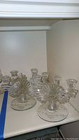 Pair of vintage Buder Bleikristall clear crystal candle holders with fan-like designs and multiple arms for candles. Displayed on white shelf.