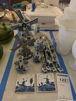 Photo showing full set of vintage Delft Blue items including windmill figurines, spoons, candlesticks, and tiles on a table with other items in background.