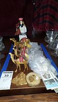 Carved wooden camels, traditional doll, various rocks wrapped in plastic, and carved wooden bowl displayed on a wooden base.