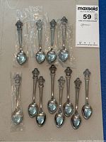 Photo of 12 vintage Rolex promotional spoons laid out on a surface, some wrapped in plastic.