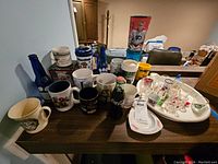 Wide overview of the mugs, bottles, shot glasses on a dark wood surface.