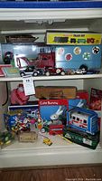 Photo showing shelves with various vintage toys including a Kubota tractor in box, tin toy cars, windup train set, and small assorted toys including a pink plush pig and a 'Cute Bunny' mechanical toy box.