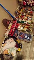 Wide view of assorted toys on floor including dolls, fire trucks, plastic figures, and the pinball machine.