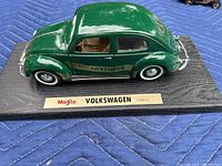 Angle view of green 1951 Volkswagen Beetle die cast model on black base showing right side and rear with labeled plaque
