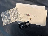 Photo showing two flight engineer wings pins in display cases, Arctic Circle crossing card with handwritten text and illustration, and a typed letter with two smaller pins.