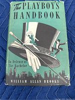 Front cover of The Playboy's Handbook showing green dust jacket with top hat, gloves, cane, and illustrated figures, city skyline at bottom, title and author in large print
