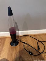 Full view of the 1990s lava lamp showing black base, black cap, clear glass cylinder with pink wax and attached electric cord with inline switch.