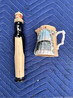 Photo showing the tall wooden clown container and ceramic Niagara Falls pitcher side by side on a blue quilted surface.