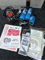 Photo showing the Badger airbrush compressor unit, three cans of airbrush chemicals, and several manuals and decal sheets spread out alongside the compressor.