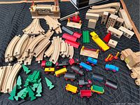 Photo showing wooden curved and straight track pieces, various wooden trains and cars, green wooden trees, and some track accessories.