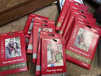 Photo showing multiple packs of Canon Photo Paper Glossy and Photo Paper Plus Glossy II in 4x6 and 5x7 sizes, stacked and arranged