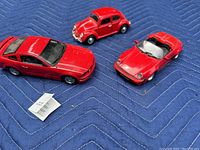 Three red die cast model cars displayed on quilted blue fabric, showing the Ford Mustang GT, Porsche 911 Speedster and Volkswagen Beetle with their details