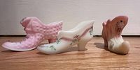 Three hand painted Fenton glass shoes in pink and white with floral patterns on wood surface