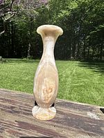 Tall Grecian-style marble vase standing outdoors on wooden surface, showing front view and natural marble veining detail.