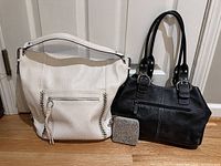 Front view of a white Jessica Simpson hobo bag, black Tignanello leather purse, and sparkly wallet displayed on floor against white door