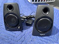 Pair of both Logitech Z130 black speakers placed on a blue surface, showing front views including volume and power knob on left speaker.