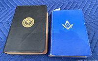 Two books placed side by side on a blue padded surface, showing covers of the Freemason Bible and Universal Handbook