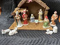 Photo of nativity set with bark-style crèche and 11 painted figurines including Holy Family, Wise Men, shepherd, and animals on padded black cloth.