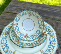 Top view showing cup in the center, placed on the saucer, salad plate, and dinner plate, displaying blue scroll and multi-colored floral design with gold trim