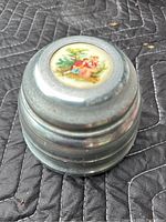 Closed view of the round powder puff music box showing the textured metal casing.