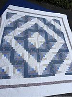 Full view of the quilted bedspread laid out flat, showing geometric patchwork pattern in blues, whites, and florals