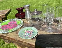 Photo showing painted glass dish, red glass bud vase, pewter bud vase, cut glass jelly jar with sterling lid, and four aperitif glasses on a wooden outdoor table.