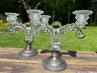 Front view of both candelabras on wood surface showing pressed glass arms and silver bases