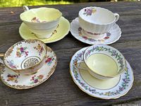 Top view of four fine bone china teacup and saucer sets resting on wood surface showing floral designs and gold accents.
