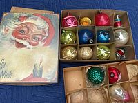 15 vintage glass Christmas ornaments in cardboard boxes, showing variety of colors and patterns with the Jolly St Nick box lid featuring Santa Claus artwork