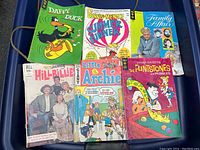 Photo showing six vintage comic books arranged in two rows on a blue surface: Daffy Duck, Dennis the Menace Summer Funner, Family Affair, Beverly Hillbillies, Little Archie, and The Flintstones Pebbles.