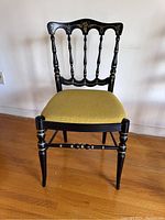 Front view of vintage black enamel Hitchcock style chair with green upholstered seat and gold detailing on the chair back and legs.