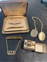 Photo showing Krementz marked tie bars in case, gold tone chain link lockets, and the Springfield high school ring in small box.