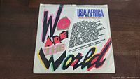 Front side of the USA For Africa We Are The World 45rpm vinyl sleeve showing title and artist names.