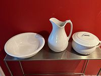 Photo showing the antique ironstone jug, bowl, and the lidded thunder pot set arranged on a shelf against a red wall.
