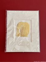 Front view of the card series print titled 'The Raven Steals the Salmon' by Bill Reid, showing the gold-colored Haida style raven design, matted and in a clear plastic sleeve.