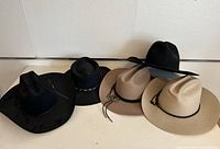 Five cowboy hats in a row, showing black and beige colors and varying brim and crown styles.