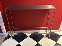 Full front view of the metal console table showing steel top and simple metal legs with horizontal foot bar.
