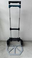 Foldable dolly cart with extended aluminum handle and metal base platform. Handles have black and teal plastic grips.