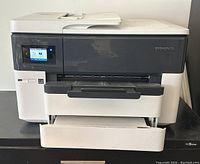 Front view of the HP OfficeJet Pro 7740 printer showing touchscreen display, opened output tray and lower paper tray, white and dark gray body.