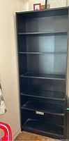 Full view of the black IKEA bookshelf showing all shelves and the outlet cutout on one shelf.