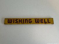 Top-down view of the rectangular metal sign with 'WISHING WELL' lettering worn around the edges showing a yellow background.