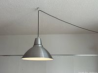 Photo of modern brushed metal hanging lamp viewed from slightly below and side angle showing the conical lampshade and suspension cord.