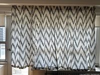 Curtains hanging in front of windows showing the zigzag grey and white chevron pattern in natural daylight, visible length and width.