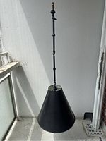 Photo showing full view of the black metal hanging lamp against a white wall, highlighting the conical shade and metal chain.