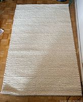 Top view of the off-white textured NuLoom rug spread on wood parquet flooring, showing full rectangular shape and knit pattern detail.