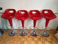 Front view of four red molded bar stools with chrome bases and footrests, showing overall condition.