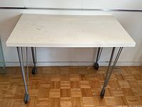 White desk with metal hairpin legs on wheels, top view showing worn surface.
