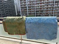 Two moving blankets hanging over balcony railing, one green with red trim, one blue with blue trim