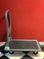 Side view of collapsible moving dolly with handle upright and platform surface visible.