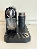 Front view of black Nespresso espresso machine with metallic lever and attached Aeroccino frother with ribbed sides.